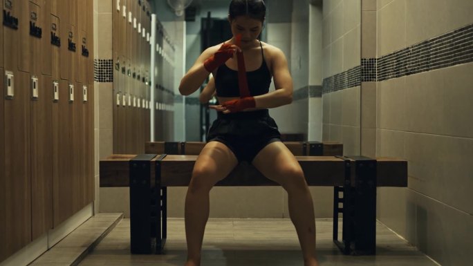 女拳手用红色的拳击绷带包扎双手，在健身房进行自由搏击训练。