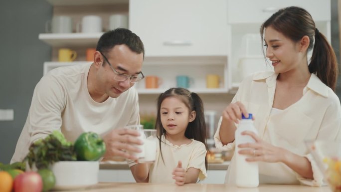 欢乐的家庭时刻:亚洲父母和孩子穿着休闲装，烹饪，在家一起享受健康的牛奶。