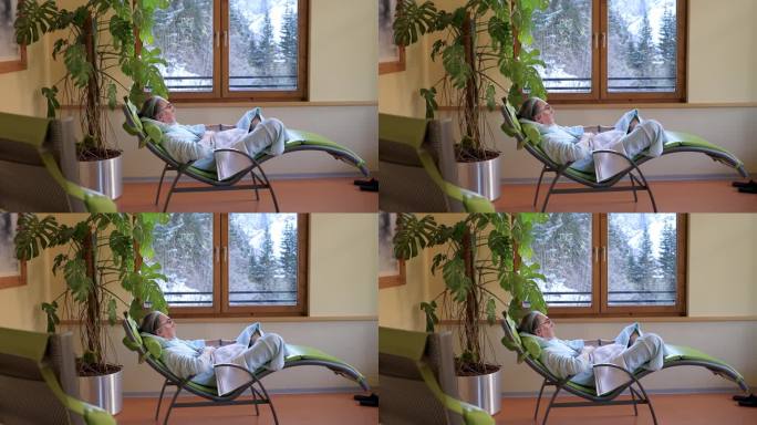 一位头发花白的男子在做完健康手术后躺在沙发上，一边做着总体规划，一边欣赏窗外的景色