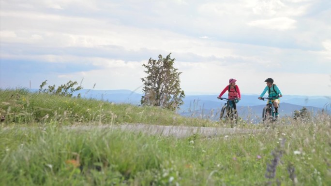 两位女性朋友骑着电动自行车沿着漂亮的山路行驶