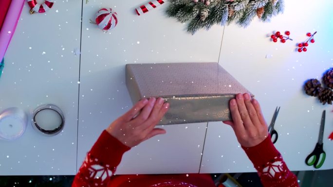 女性双手用纸包好圣诞礼盒，放在带有装饰元素的白色桌子上