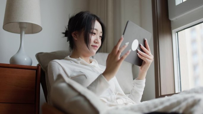 年轻的亚洲女性在家里使用数字平板电脑购物