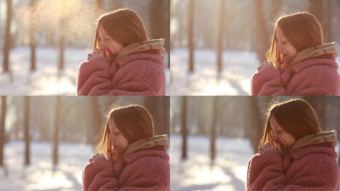 在冬天的公园里，美丽的年轻女子试图用呼吸温暖她冻伤的手。在冰天雪地的户外，呼吸着霜冻的女孩享受着寒冷