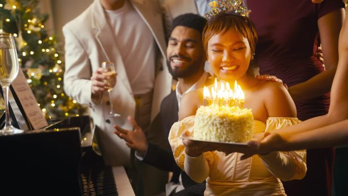 一群朋友围着钢琴庆祝女人的生日，吹灭蛋糕上的蜡烛