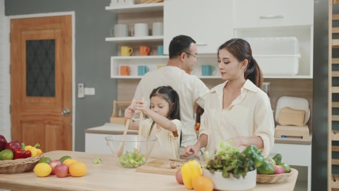 微笑的亚洲家庭通过厨房的烹饪乐趣:父母教孩子准备新鲜蔬菜沙拉的艺术。