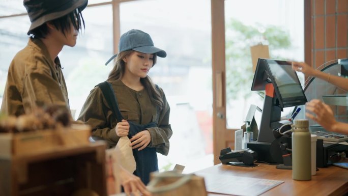 在一家环保咖啡店里，两名亚洲顾客点饮料，一名咖啡师接单。