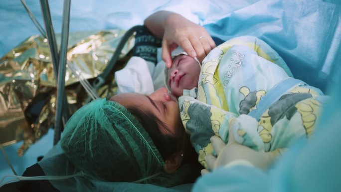 医院里母亲抱着刚出生的婴儿。刚分娩的母亲把刚出生的婴儿抱在胸前。第一眼看到手术室里的妈妈和她的新生儿