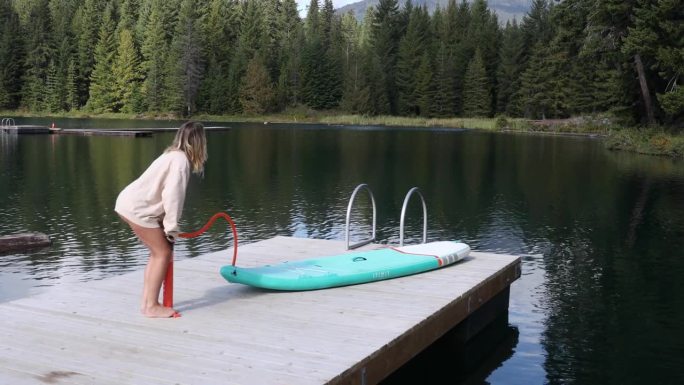 女子在宁静的湖码头吹桨板(SUP)