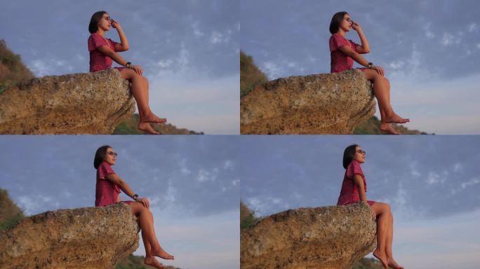 一个快乐的女人，戴着墨镜，坐在一块石头上，背景是天空