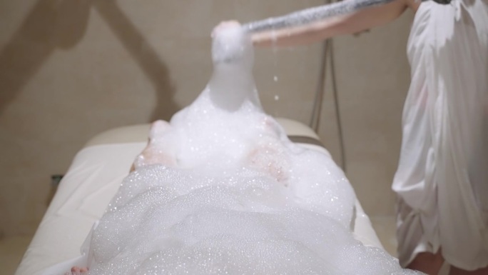 在土耳其浴室里，水疗中心的工作人员在泡沫肥皂泡沫下用水流给女人洗澡。女性放松，接受身体皮肤治疗、清洁