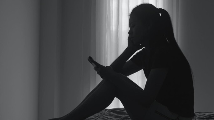 患有抑郁症和抑郁症的女性在房间里使用智能手机的剪影，悲伤，焦虑，家庭问题，精神病患者，家庭暴力