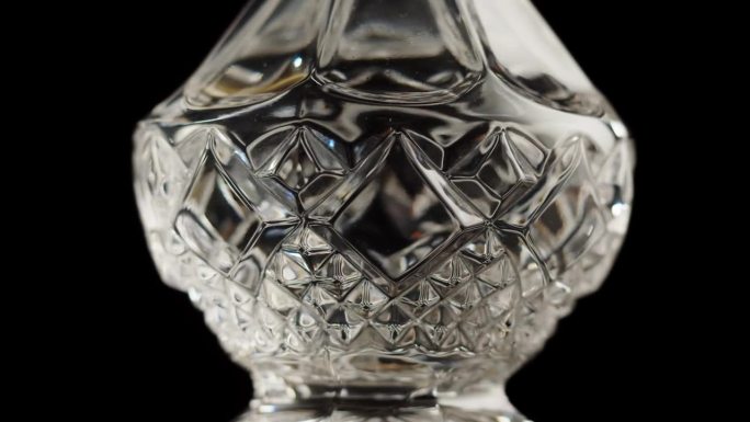 空水晶酒瓶特写。透明玻璃在黑色背景上旋转。高档酒瓶，酒精饮料，玻璃器皿。