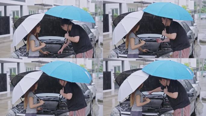 一名亚洲妇女和她的男邻居打着伞，站在大雨中，站在一辆坏掉的汽车前，汽车盖打开，停在一个村庄的路边，因