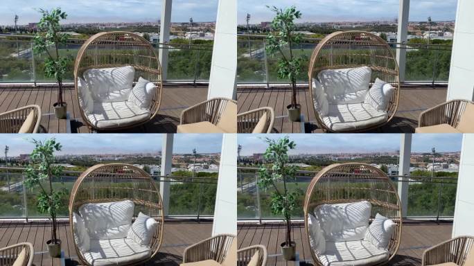 阳台上的藤蛋椅，白色靠垫和枕头，俯瞰城市。