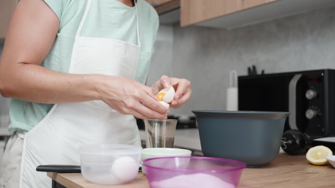 一个女人正在明亮的厨房里做饭。她打了一个鸡蛋，把蛋清和蛋黄分开放进玻璃杯里。