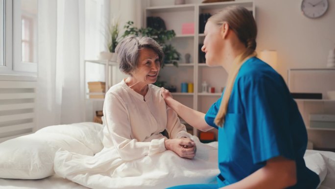 关怀护士在医院病房与积极的老年女病人交谈