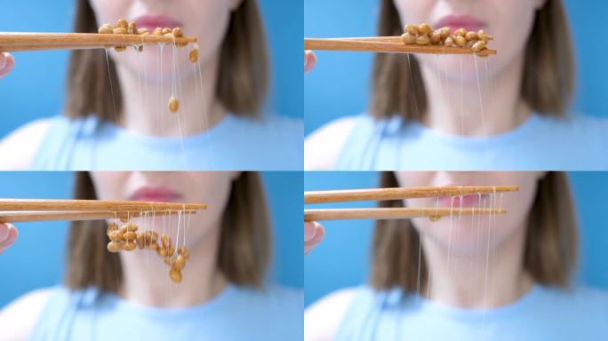 年轻女子用木筷子吃日本纳豆(正面特写，蓝色背景)。