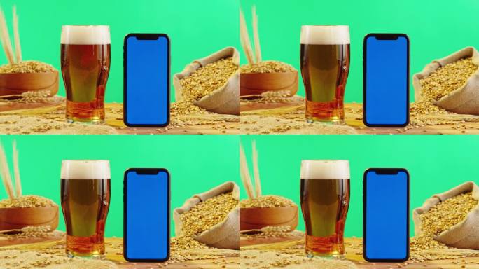 泡沫啤酒在玻璃和手机与蓝色色度键屏幕。酒精金色啤酒杯喝。绿色背景下的新鲜淡啤酒。