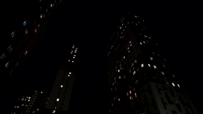 夜景高层住宅，窗户透光。行动。夏夜静悄悄的城市，底层看住宅楼。