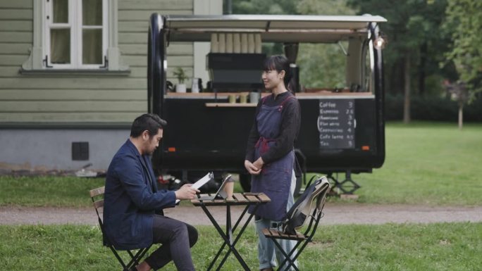 日本咖啡师正在接受坐在她的咖啡拖车旁的顾客的订单