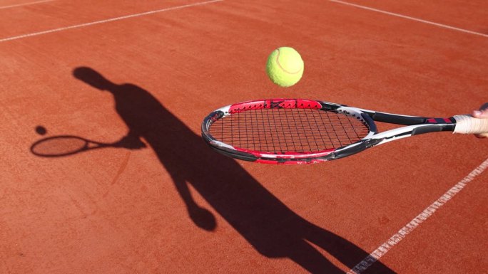 少年在网球拍上轻拍球。他在红土场上练习网球，慢动作