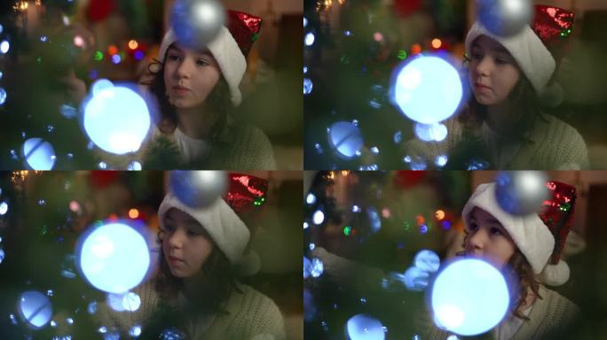 特写镜头。一个戴着圣诞帽的女孩在圣诞树上精心挑选圣诞球。