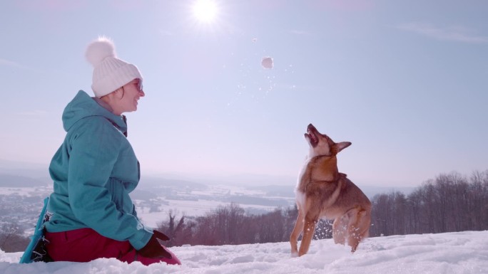 慢镜头，特写:微笑的女人向她可爱的顽皮的狗扔雪球
