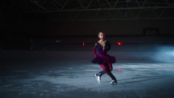 年轻女子花样滑冰运动员在黑暗中的冰场强化训练，为比赛做准备
