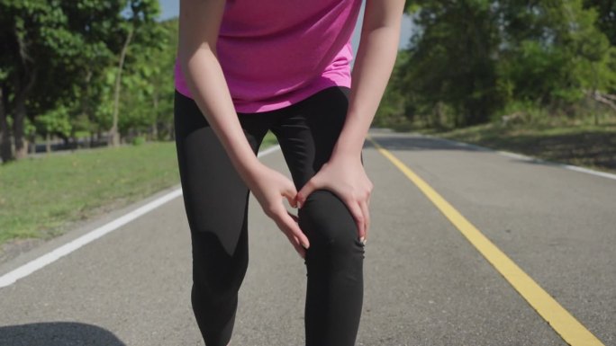 在一个阳光明媚的日子里，年轻的女跑步者在当地的一个跑步公园跑步后腿部和膝盖疼痛