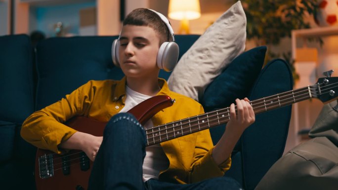 十几岁的男孩戴着耳机在家里弹贝斯吉他，音乐爱好
