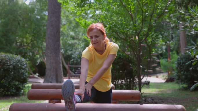 健康的中年成年妇女在自然公园的木栏上伸展双腿