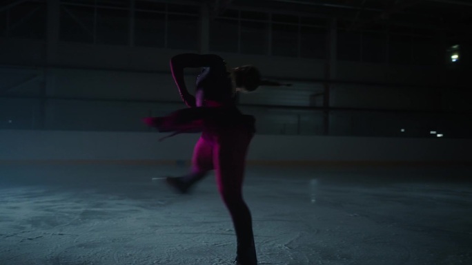 黑暗中溜冰场上优雅的女滑冰者的剪影，女士旋转，慢动作镜头