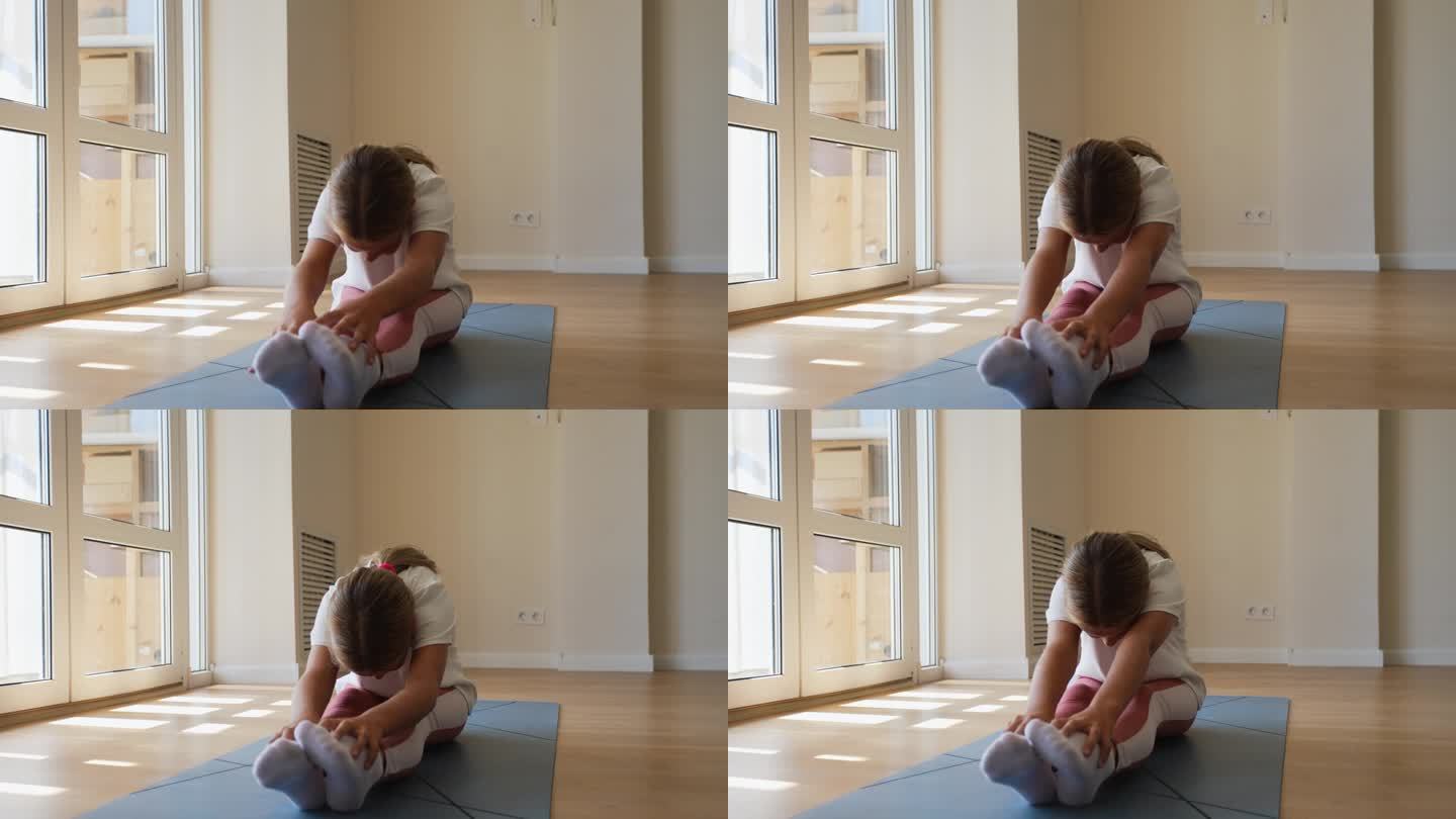 柔韧的小女孩坐在地板上伸展向前弯曲保持脚趾尽可能长。孩子在做伸展运动弯曲的肖像