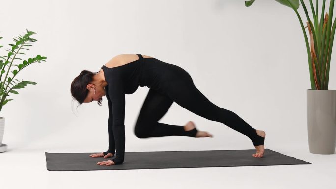 深色头发的女人在练习瑜伽，做查图兰加丹达体式运动，动态平板支撑，在工作室的垫子上穿着一件黑色运动工作