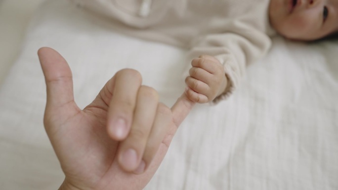 一个小女孩躺在床上看着她的妈妈，握着她的小手指。