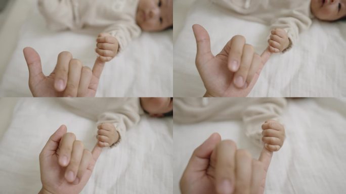 一个小女孩躺在床上看着她的妈妈，握着她的小手指。