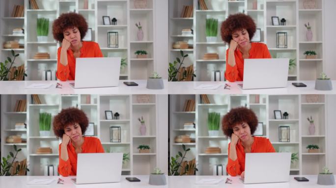 疲惫的非裔美国女性坐在办公桌前的无线笔记本电脑前感到困倦和无聊。缺乏动力，工作观念单调乏味。