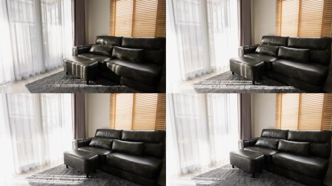 在安静的客厅里，明亮的阳光透过玻璃门和白色的窗帘照在黑色的沙发上。