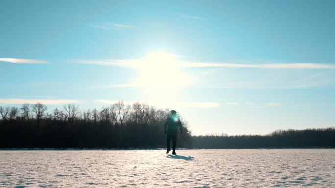 一个男人的剪影在夕阳下穿过雪地走向远方。一个孤独的人走过一片大雪覆盖的草地。失败和孤独。
