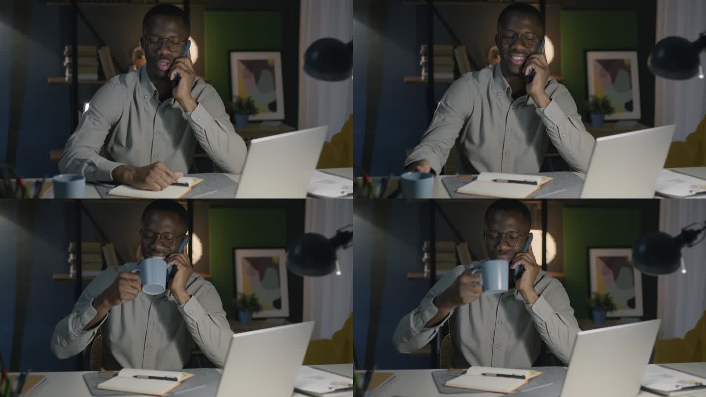 一个非洲裔美国人晚上坐在办公室的办公桌前一边打电话一边喝茶