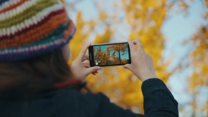 女子用手机拍摄秋天的景色