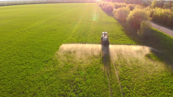 拖拉机春季在田间喷洒土壤和幼嫩作物的航拍视频。春天，拖拉机用喷雾器在大豆地里喷洒农药。拖拉机喷水器的