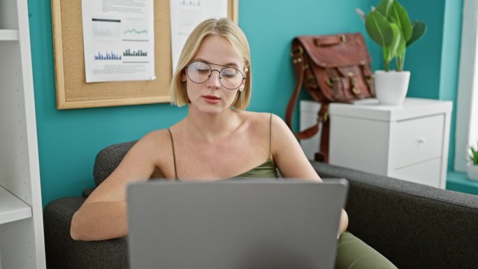 年轻的金发女商务工作者在办公室用笔记本电脑看手表