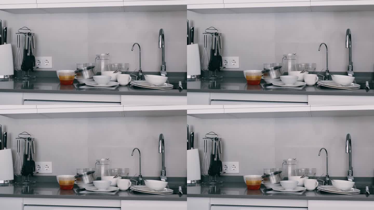 白色的脏盘子在灰色的现代厨房水槽旁，厨房里乱七八糟，单色，在家里洗厨具。杯子,盘子