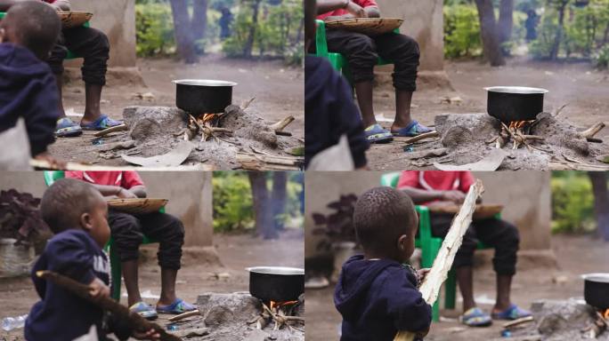 小男孩拿着柴火的慢动作。食物正在柴炉上煮着。他们在后院。