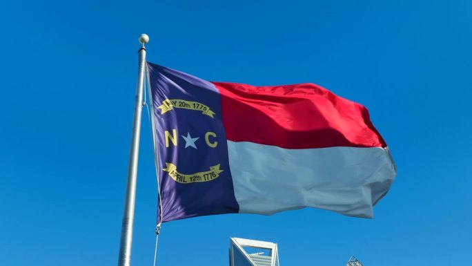 北卡罗来纳州的国旗在明亮的蓝天上飘扬。北卡罗来纳州市中心的静态航拍照片。