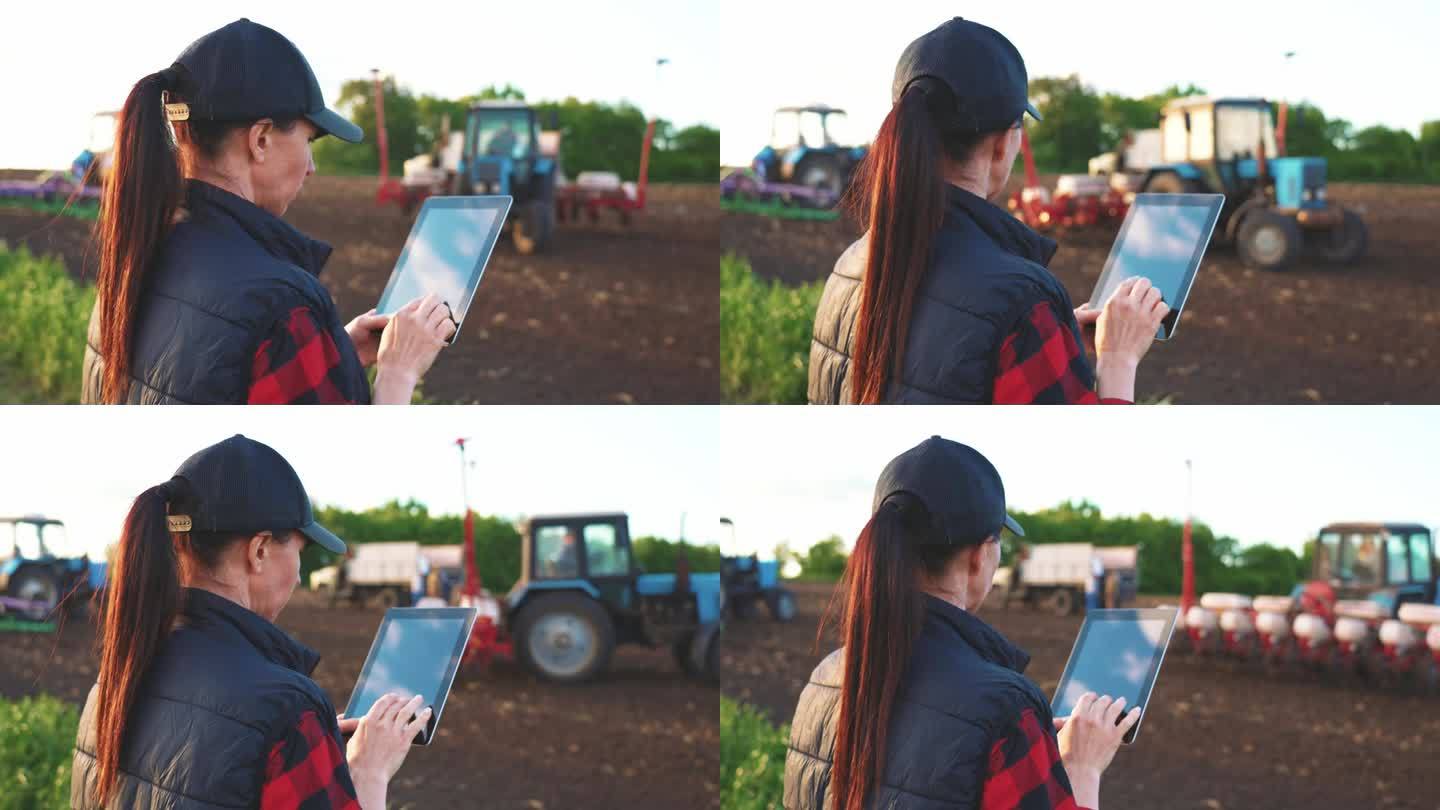 妇女在田间工作拖拉机的背景下，在平板电脑上使用专门的应用程序。农田遥控机械设备。小企业工作理念优化。