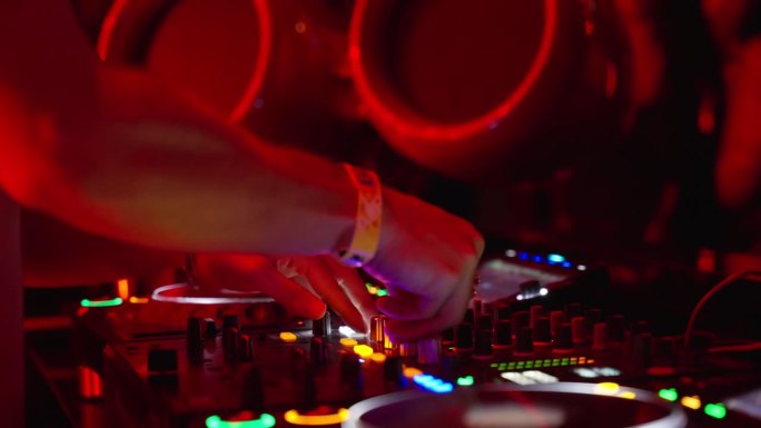 DJ正在夜总会的霓虹灯下调节数字音乐控制台的音量。