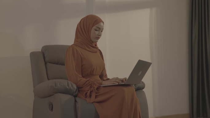 戴头巾的穆斯林妇女在家里使用笔记本电脑，人们信仰伊斯兰教的生活方式概念。