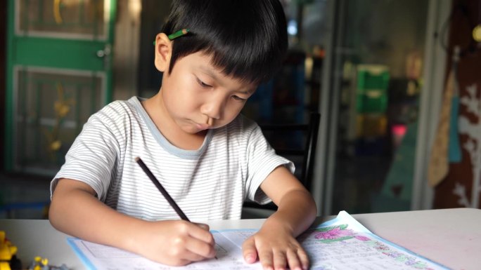 亚洲小男孩坐在课桌前写练习本。可爱的小学生在家里做作业，脸上带着微笑和专注。教育理念，学习，家校。